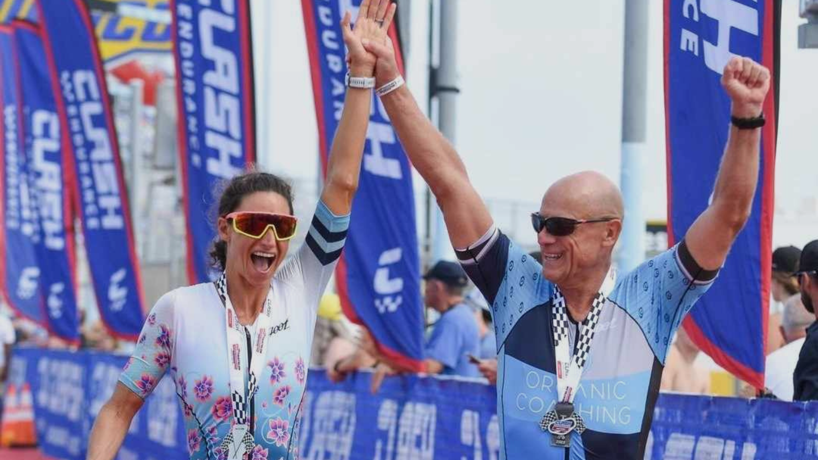 man and woman crossing triathlon finish line with arms raised in the air
