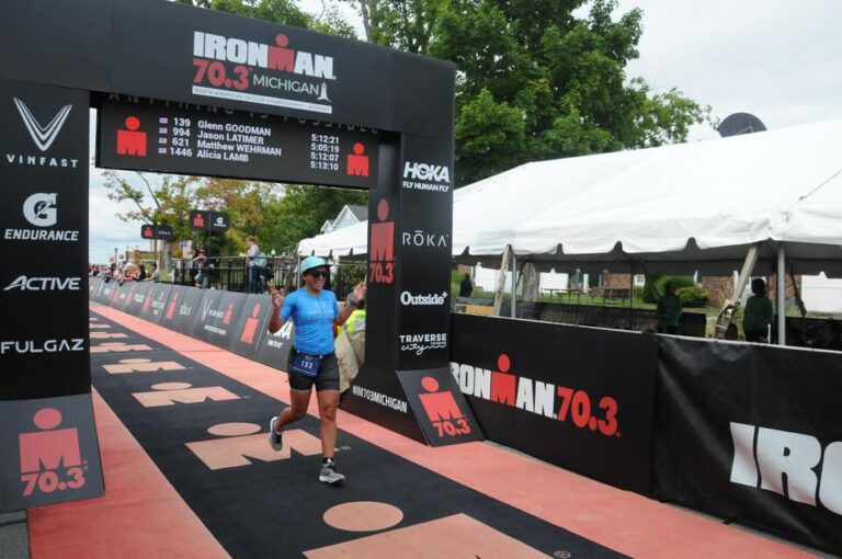 Woman crossing the finishline of Ironman 70.3 Michigan. Happy.